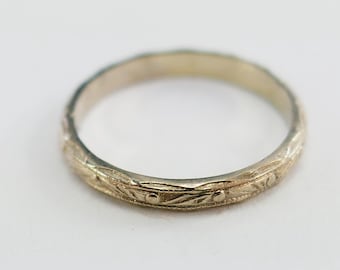 May include: A gold-colored ring with an engraved floral pattern. The ring has a thin band and a detailed design of leaves and small dots. The ring is likely made of metal and is a piece of jewelry.