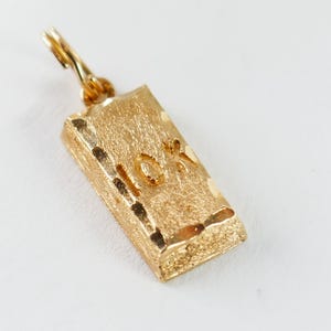 May include: Gold-colored charm shaped like a gold bar with a textured surface and the inscription "10K" on the front.