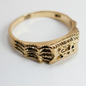 May include: A gold ring with a textured band and a rectangular top featuring the letters "SA".