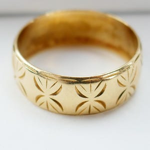 May include: A gold band ring with a detailed, engraved pattern of repeating starbursts.