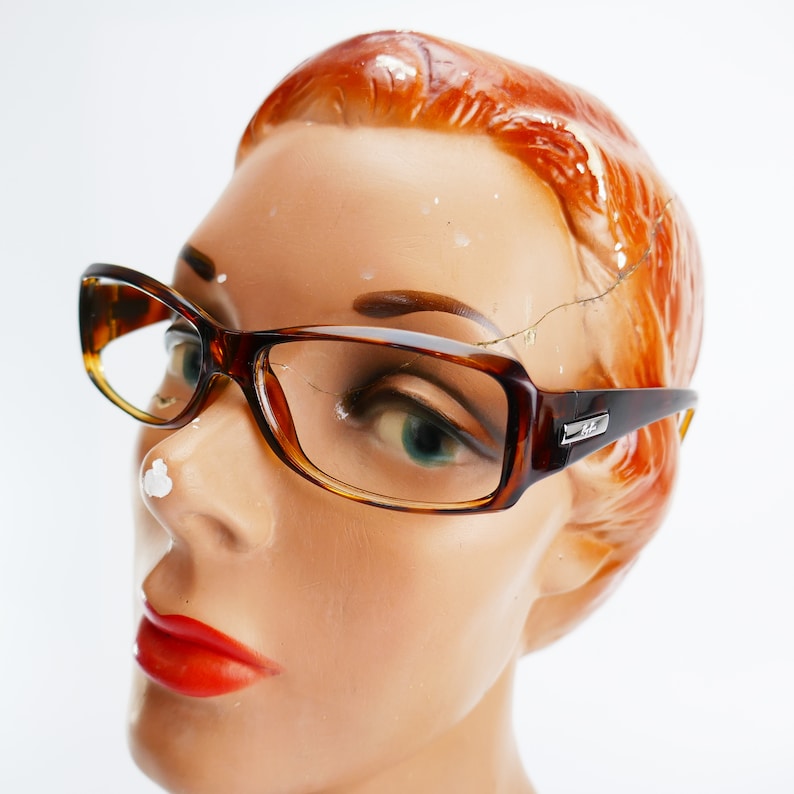 Peut inclure: Une monture de lunettes en &eacute;caille de tortue brune avec des verres transparents. Les lunettes sont sur une t&ecirc;te de mannequin avec des cheveux roux.