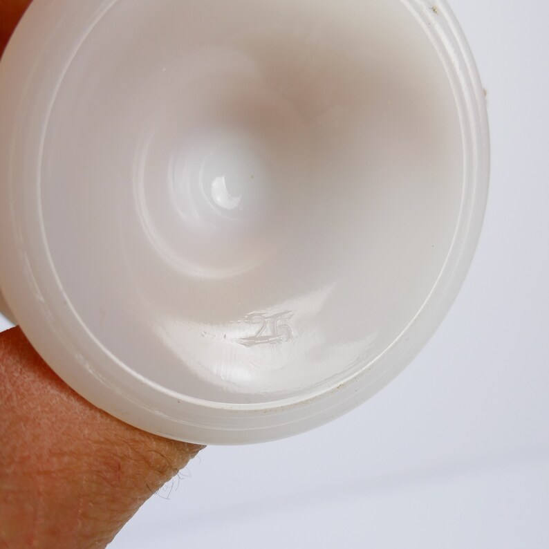 May include: A white, opaque glass pedestal bowl, viewed from above, with a rounded base and a flared rim. The bowl has a smooth, glossy surface. The number "25" is etched on the bottom of the bowl.