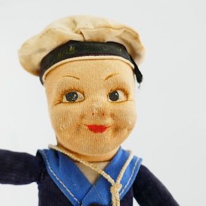 Peut inclure: Poupée de marin vintage avec un visage en tissu, des yeux peints et un sourire peint en rouge. La poupée porte un costume de marin bleu marine avec un col blanc et un chapeau de marin assorti avec une bande noire.