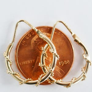 May include: A pair of gold hoop earrings with a twisted rope design. The earrings are shown next to a penny for size comparison. The penny is dated 1988.