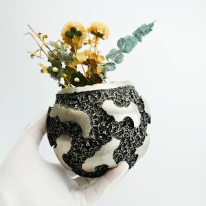 May include: A black and silver textured ceramic vase with a bouquet of dried yellow and green flowers.