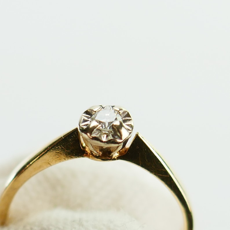 K&ouml;nnte beinhalten: Ein goldener Ring mit einem einzelnen, klaren Diamanten in einer Krappenfassung.