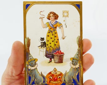 Könnte beinhalten: Vintage Halloween-Postkarte mit goldenem Rand. Sie zeigt eine Frau in einem gelben Kleid mit schwarzen Katzenmotiven, einen Kürbis und schwarze Katzen mit Hüten. Das Wort "HALLOWE'EN" steht unten.