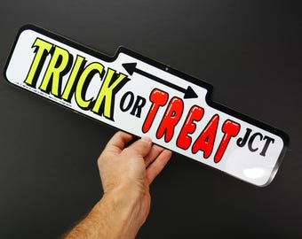Könnte beinhalten: Ein weißes Schild mit schwarzem Rand und Pfeilen, die in entgegengesetzte Richtungen zeigen. Das Schild lautet "Trick or Treat JCT" in schwarzen und roten Buchstaben.