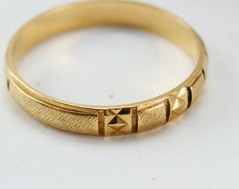 Könnte beinhalten: Ein goldfarbener Ring mit strukturierter Oberfläche und geometrischen Mustern. Der Ring weist rechteckige und rautenförmige Designs um das Band auf. Der Ring ist vor einem weißen Hintergrund platziert.