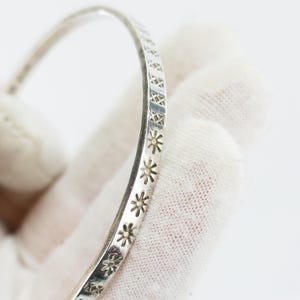 May include: A silver bracelet featuring a repeating pattern of star and geometric shapes. The bracelet is curved and appears to be made of metal. The design is etched into the surface, creating a textured appearance. The bracelet is shown against a white background.