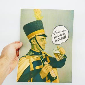 May include: Vintage advertisement featuring a man in a military uniform holding a bottle and a mug of beer. The ad includes the text "Pour moi TOUJOURS MOLSON" in a speech bubble. The uniform is navy blue with gold accents.