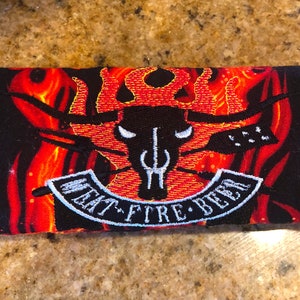 May include: A black and red fabric pouch with a flame design. The pouch has a white embroidered patch with the text "Eat - Fire - Beer".