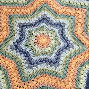 May include: A handmade, star-shaped crochet blanket in a variety of pastel colors. The blanket features a central star design with concentric rings of peach, blue, green, and yellow. The crochet stitches create a textured, detailed pattern.