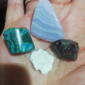 May include: Assortment of polished gemstones in various shapes and colors. Includes a large, triangular blue lace agate, a green and blue malachite, a dark green stone with teal accents, and a small, white, irregularly shaped stone.