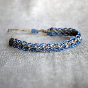 Può includere: Braccialetto in macramè fatto a mano con un motivo intrecciato nei toni del blu e beige. Il braccialetto è realizzato con cordoncino in fibra naturale e ha una chiusura regolabile. Un accessorio artigianale per l'uso quotidiano.