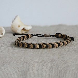 Peut inclure: Un bracelet d'amitié tressé noir et beige. Le bracelet est fait de fines cordes tissées ensemble en un motif.
