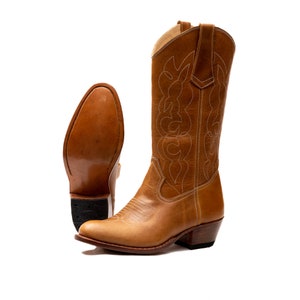 May include: A pair of brown leather cowboy boots with a pointed toe and a low heel. The boots have a decorative stitching pattern on the shaft.