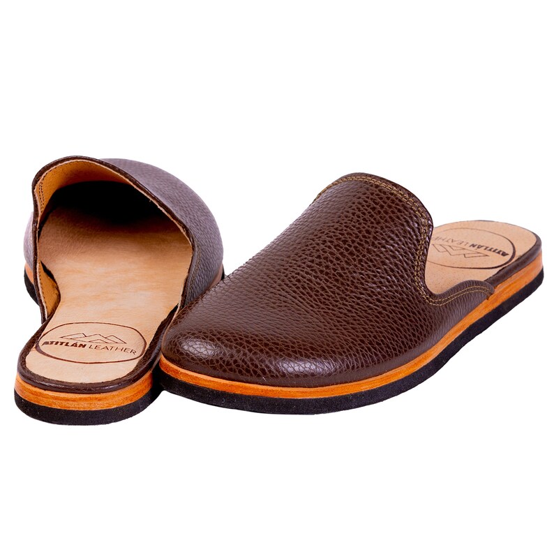 May include: A pair of brown leather slip-on shoes. The shoes have a textured surface and a light brown sole with a black and orange trim. The interior is light brown, and the brand name "ATITLAN LEATHER" is visible.