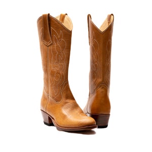 May include: A pair of tan leather cowboy boots with white stitching. The boots have a pointed toe and a low heel.
