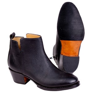May include: Black leather ankle boots with a side zipper and a stacked heel. The boots have a rounded toe and a pull tab at the back. The sole is black rubber with a brown leather heel.