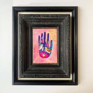 May include: A framed painting of a hand with a pink background. The hand is blue and has a floral design with three birds. The birds are yellow, blue, and white.