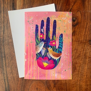 May include: A pink and blue hand with flowers and birds. The hand is painted in a whimsical style with bright colors and details. The birds are perched on the flowers and are looking at each other.