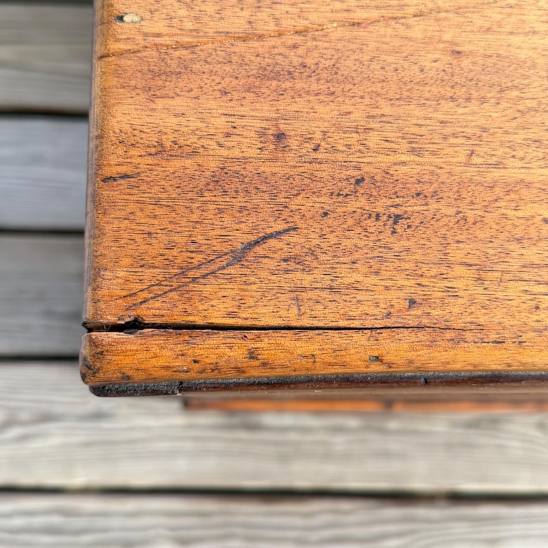 May include: Close-up of a wooden surface with a warm, reddish-brown hue. The wood grain is visible, with natural variations in color and texture. The corner of the wooden object is visible, showing the edge and the way the wood pieces are joined.