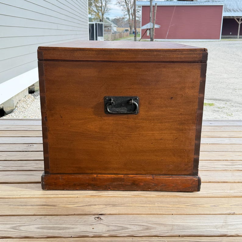 May include: A rectangular wooden chest with a dark brown finish. It features a metal handle and a base. The chest is likely used for storage and has a classic, vintage appearance. The wood grain is visible.