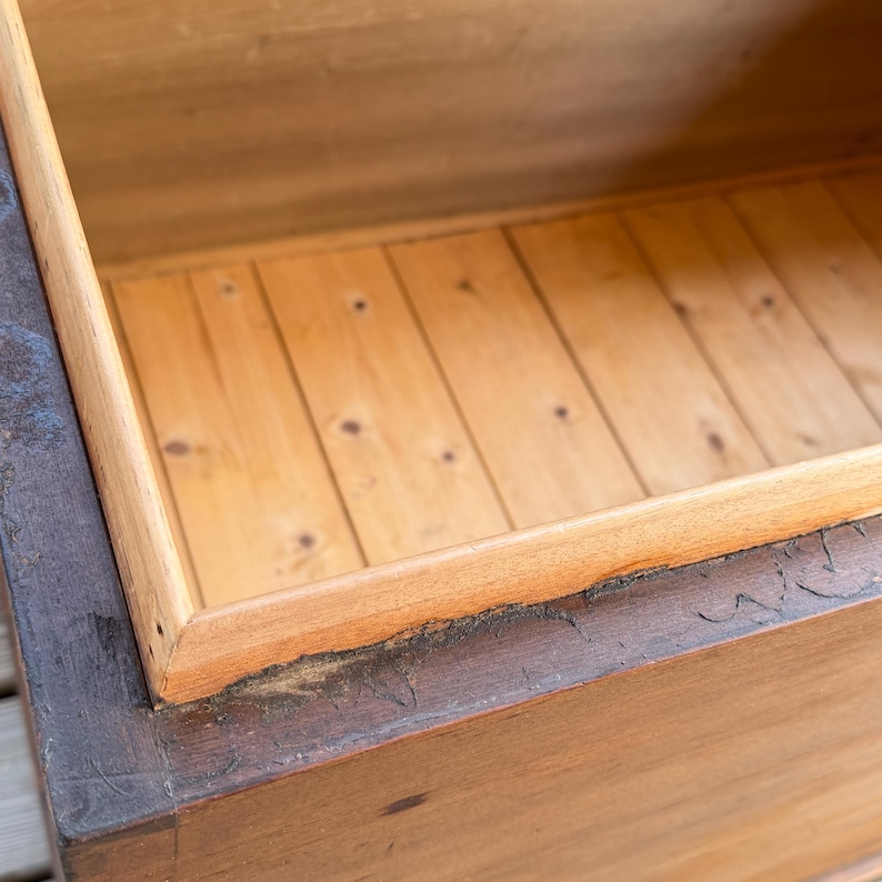 May include: An open wooden chest with a light brown interior and a darker brown exterior frame. The interior features wooden planks, and the frame shows signs of age and wear. The chest appears to be empty.