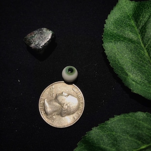 May include: A silver US quarter with the year 1971 and the words "In God We Trust" and "Liberty" on it. A green and white glass eye and a dark green rock are also in the image.