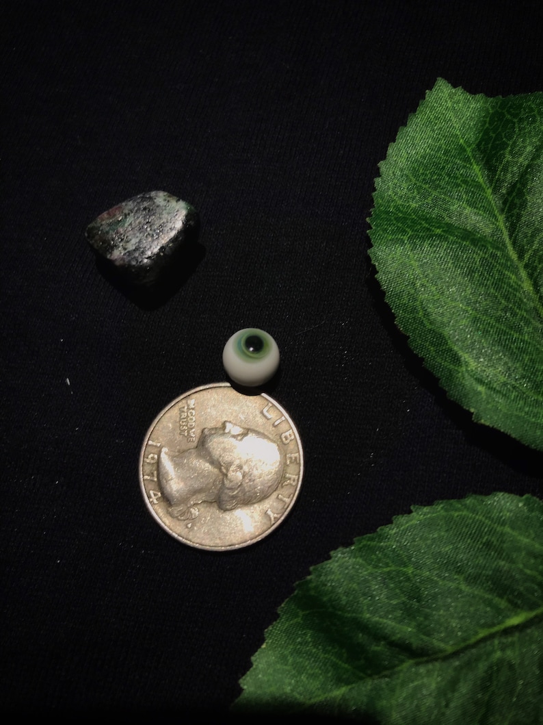 May include: A silver US quarter with the year 1971 and the words "In God We Trust" and "Liberty" on it. A green and white glass eye and a dark green rock are also in the image.