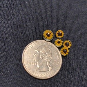 May include: Five small glass beads with a sunflower design. The beads are yellow and brown and are about the size of a US quarter.