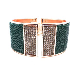 Peut inclure: Un bracelet jonc vert et or avec un motif décoratif de strass transparents. Le bracelet est en cuir et possède une fermeture à charnière.