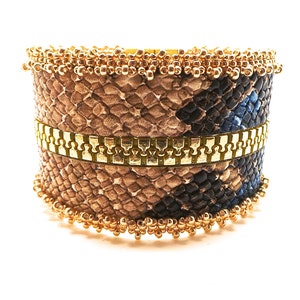 May include: A gold and brown snakeskin bracelet with a gold zipper detail and gold bead trim.