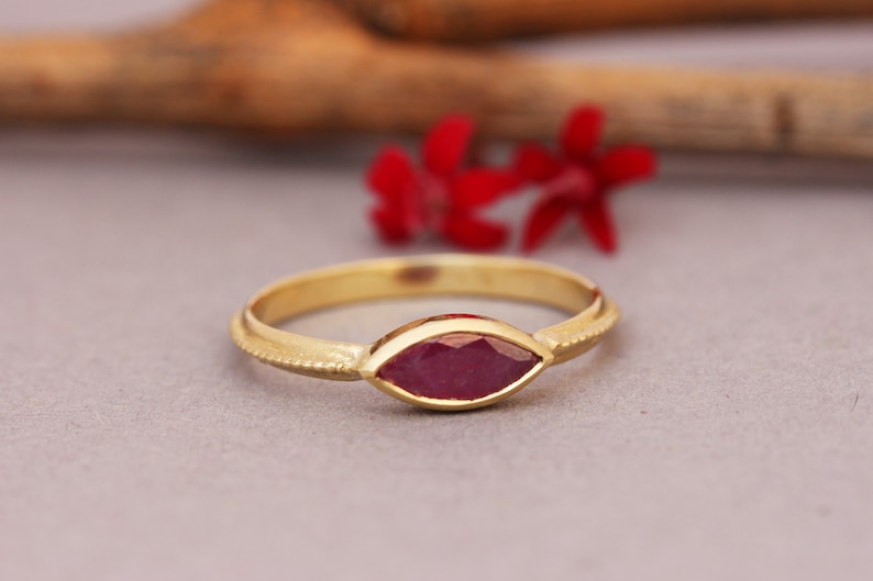 Op de afbeelding: Een gouden ring met een marquise-vormige robijn. De ring heeft een getextureerde band.