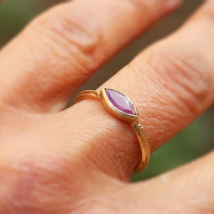 Op de afbeelding: Een gouden ring met een markiesvormige paarse edelsteen.