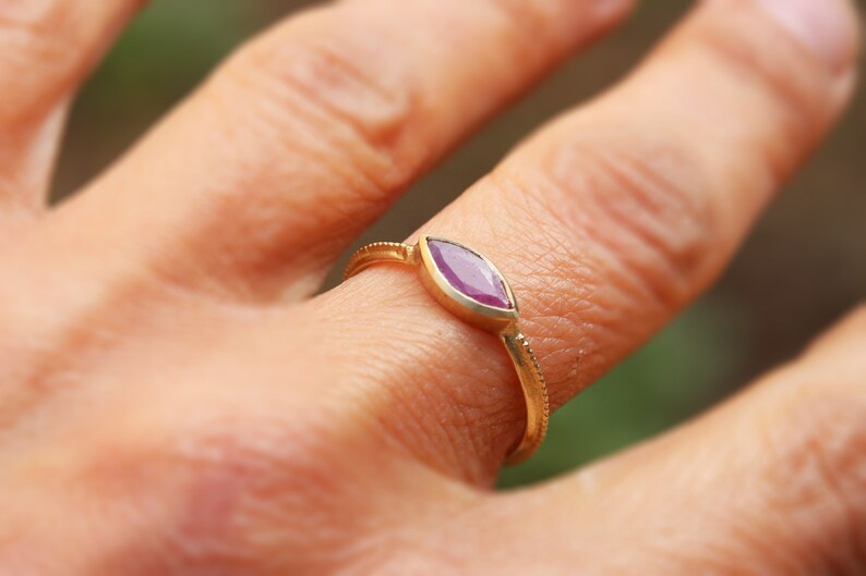 Op de afbeelding: Een gouden ring met een markiesvormige paarse edelsteen.