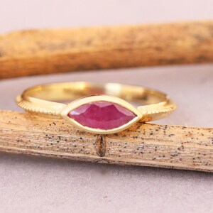 Op de afbeelding: Een gouden ring met een marquise-vormige robijn. De ring heeft een getextureerde band.
