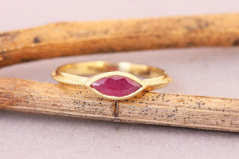 Op de afbeelding: Een gouden ring met een marquise-vormige robijn. De ring heeft een getextureerde band.
