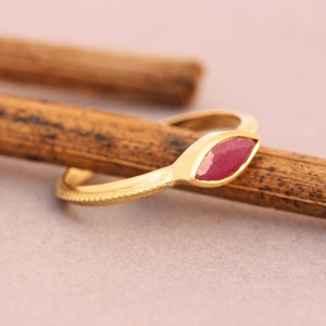 Op de afbeelding: Een gouden ring met een markiesvormige robijn in het midden. De ring ligt op een houten oppervlak.