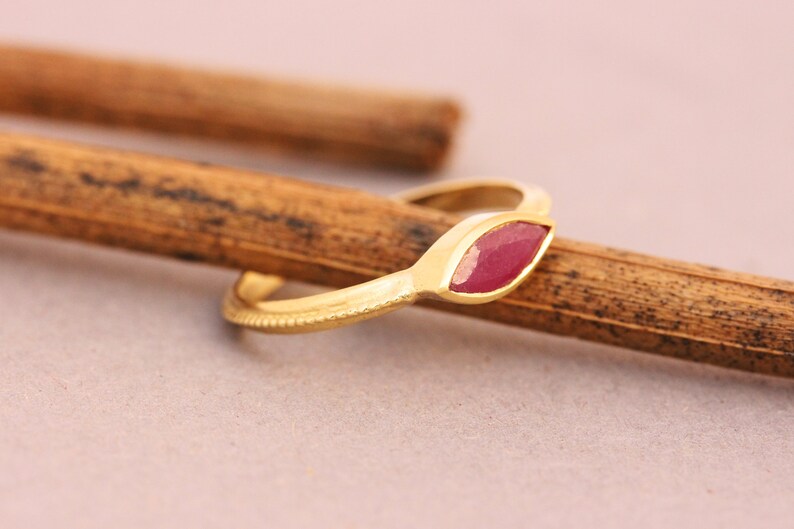 Op de afbeelding: Een gouden ring met een markiesvormige robijn in het midden. De ring ligt op een houten oppervlak.