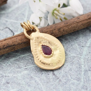 May include: A gold pendant with a hammered texture and a red gemstone in the center.