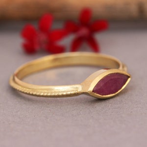 Op de afbeelding: Een gouden ring met een marquise-vormige robijn. De ring heeft een delicate, getextureerde band.