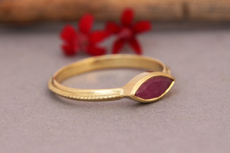 Op de afbeelding: Een gouden ring met een marquise-vormige robijn. De ring heeft een delicate, getextureerde band.
