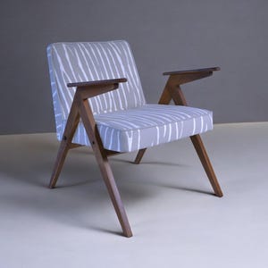 Può includere: Una poltrona moderna di metà secolo con seduta e schienale grigio chiaro con motivo a righe bianche. La sedia ha braccioli e gambe in legno. Il telaio è in legno.
