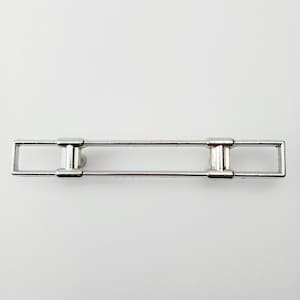 May include: A silver-colored metal tie bar with a rectangular design. The tie bar has a central bar with two rectangular ends and two vertical supports. The tie bar is designed to keep a tie in place.