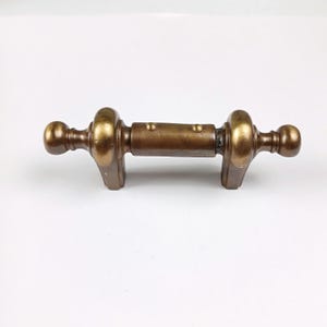 May include: A brass door handle with a rounded design and a smooth finish. The handle has two knobs on either end and a central bar.