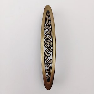 May include: A decorative, elongated bronze-colored cabinet pull with an intricate openwork design. The design features repeating scroll-like shapes and a central floral motif. The pull is approximately 6 inches long.
