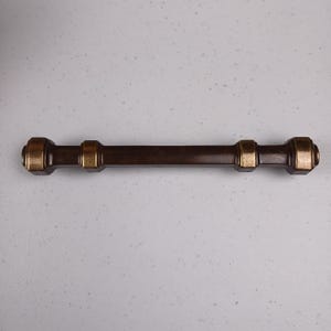 May include: A dark brown wooden drawer pull with gold accents. The pull has a cylindrical shape with rounded ends and two gold bands in the centre.