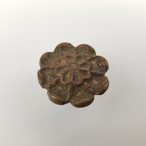 May include: A gold-toned metal button with a flower design. The button has a raised, detailed floral pattern.